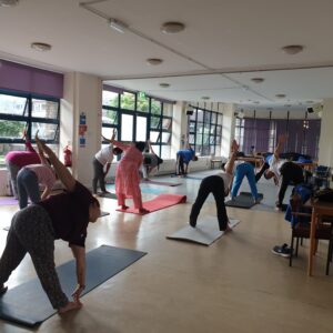 A group of people stretching on mats in a hall full of windows to one side. They're bending over to touch their toes.