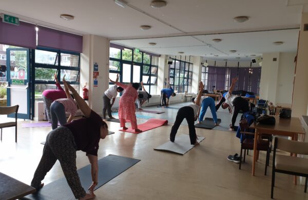 A group of people stretching on mats in a hall full of windows to one side. They're bending over to touch their toes.