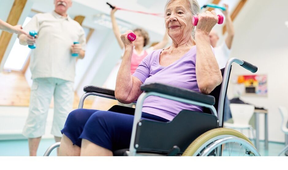 A group pf older adults, some are seated and some standing. They are using small weights and bands to complete upper body exercises.