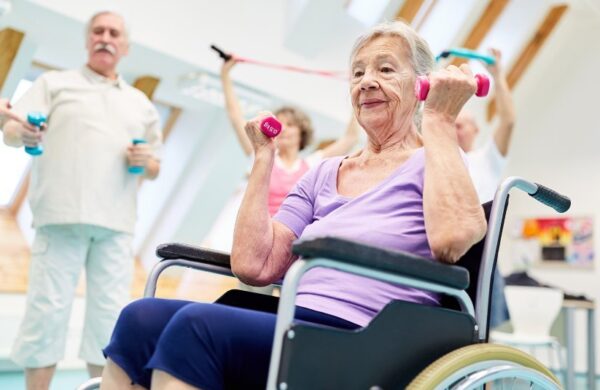 A group pf older adults, some are seated and some standing. They are using small weights and bands to complete upper body exercises.