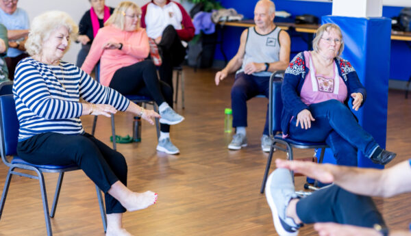 A group of older ladies sat doing chair based exercise in a circle.