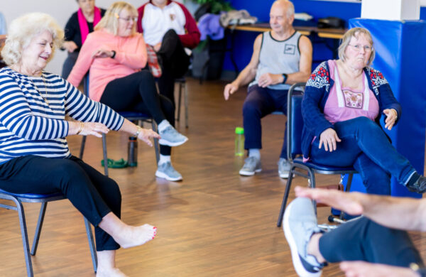 A group of older ladies sat doing chair based exercise in a circle.